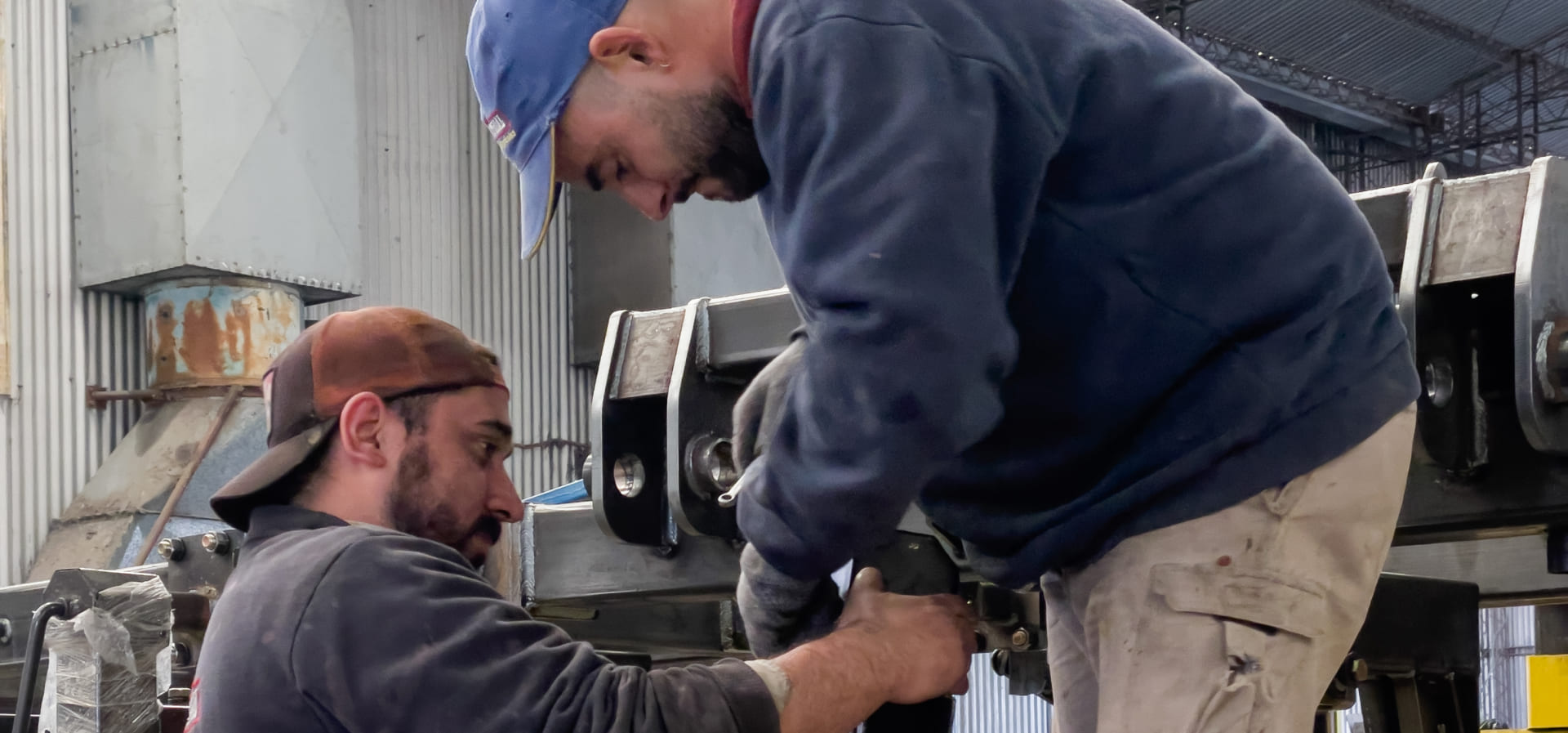 Hombres trabajando sobre carpidor para unir una pieza de acero